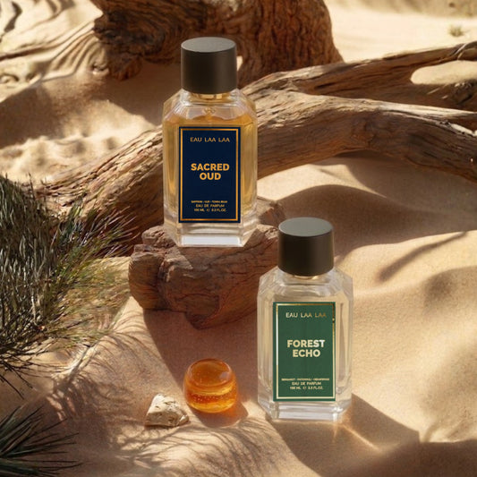 Two perfume bottles labeled 'Sacred Oud' and 'Forest Echo' on a sandy surface with natural elements.