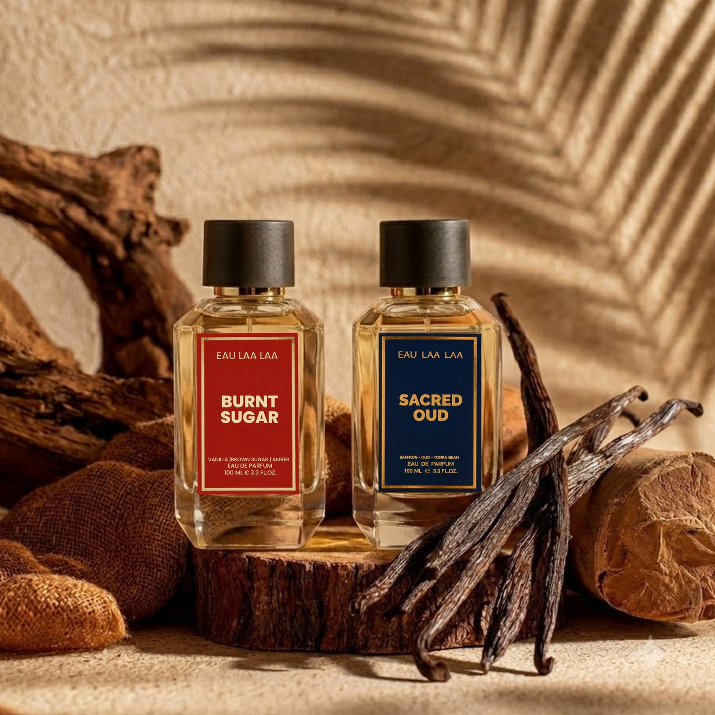 Two perfume bottles labeled 'Burnt Sugar' and 'Sacred Oud' on a wooden surface with vanilla beans.