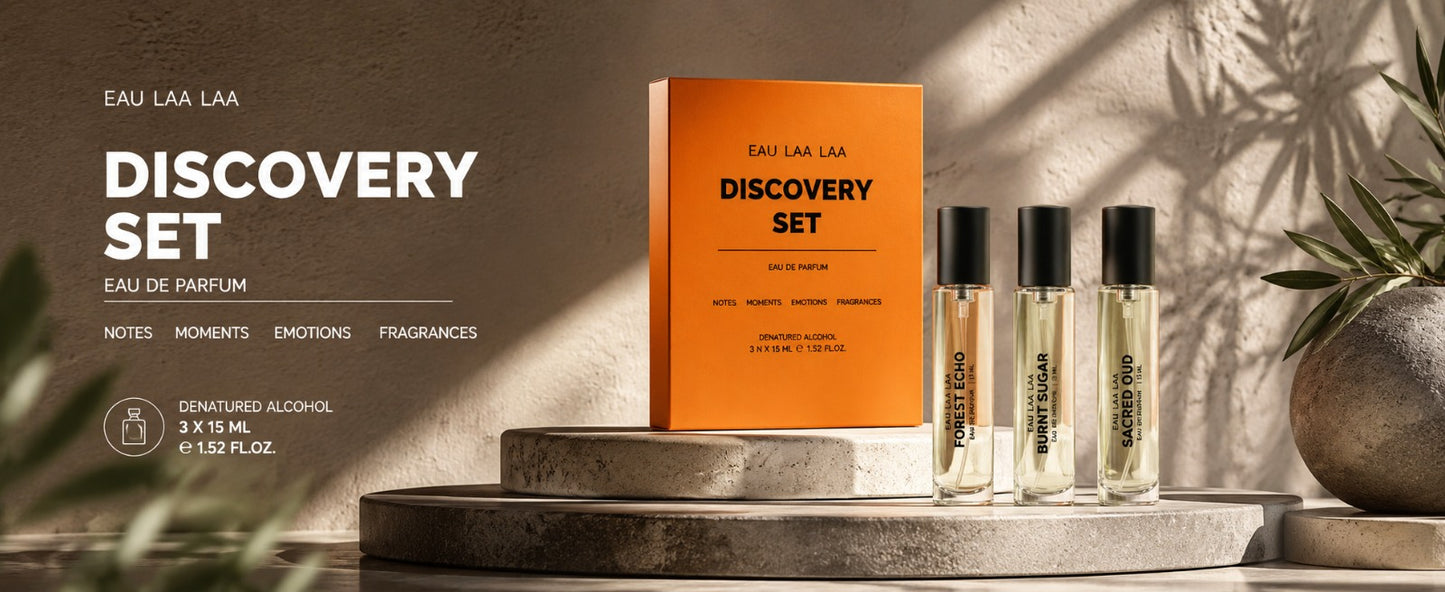 Eau Laa Laa Discovery Set perfume, featuring an orange box and three clear glass bottles with black caps, displayed on stone pedestals with warm, shadowed lighting.