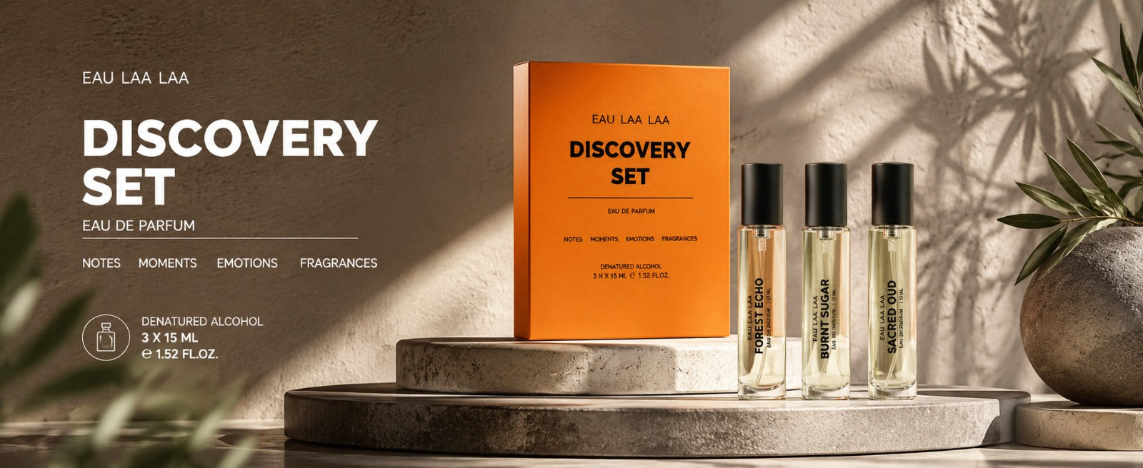 Eau Laa Laa Discovery Set perfume, featuring an orange box and three clear glass bottles with black caps, displayed on stone pedestals with warm, shadowed lighting.